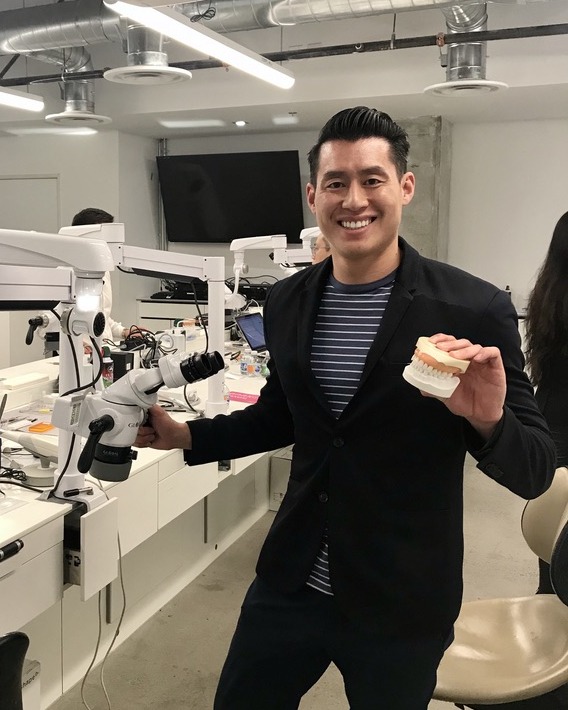 Dr. Brian Diep holding a dental model in a microscope training lab